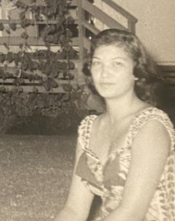 A woman in a patterned vintage dress relaxes in a garden on a sunny afternoon.