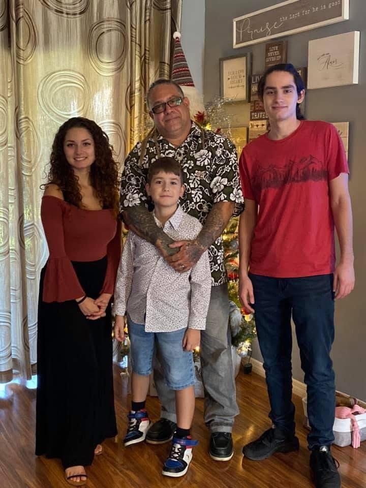 A family stands together, smiling in a warmly decorated living room during the holidays.