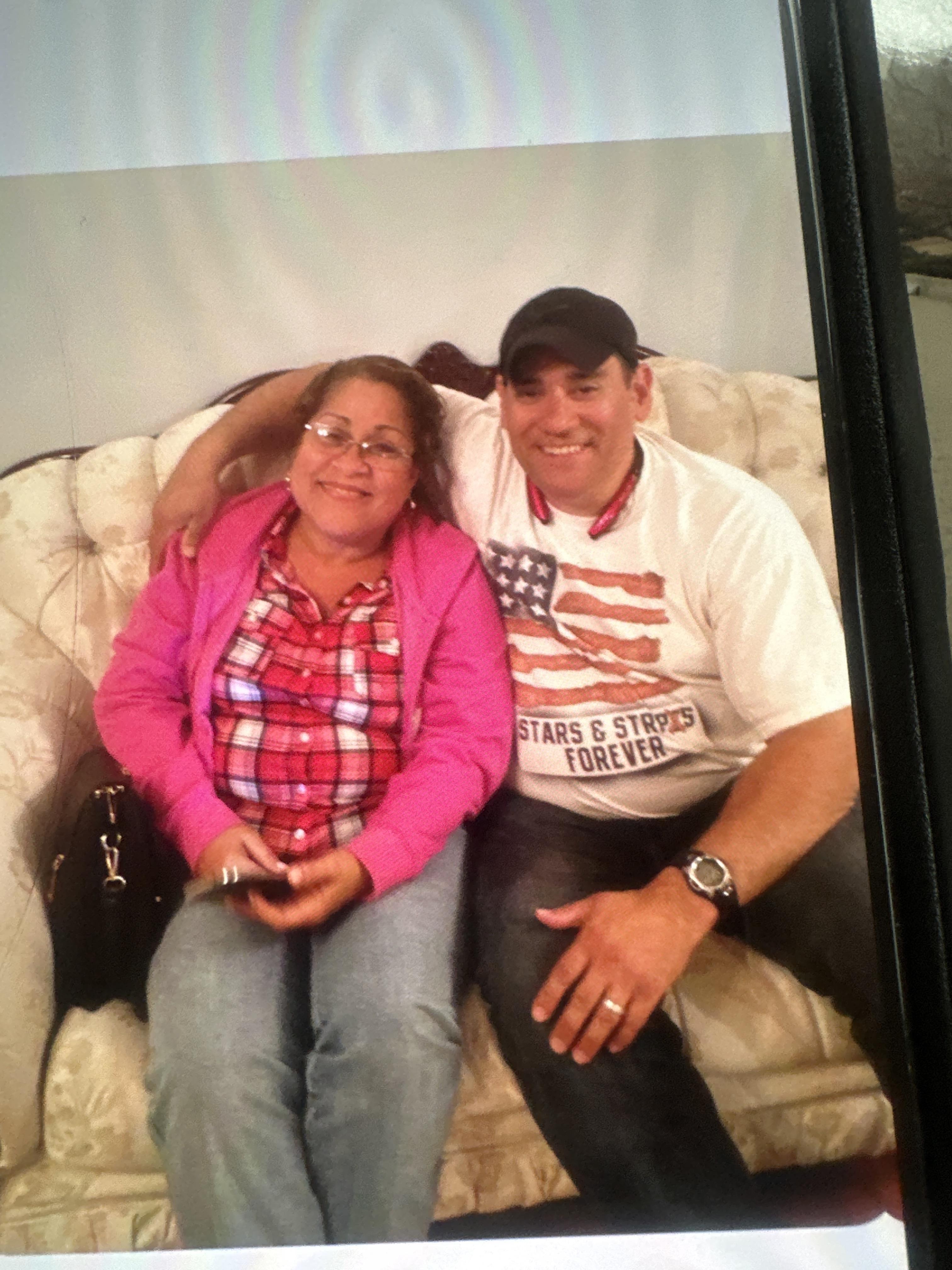 A couple happily poses on a cozy couch, enjoying their time together at a casual gathering.