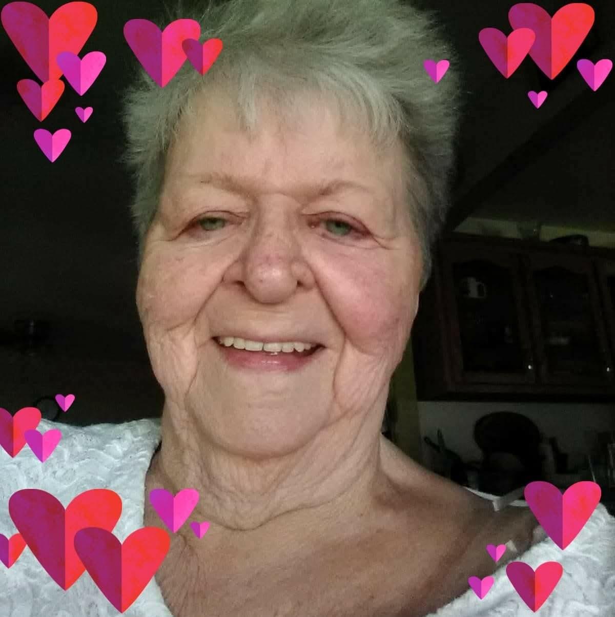 Joyful older woman smiles warmly as colorful hearts surround her in a cozy living room.