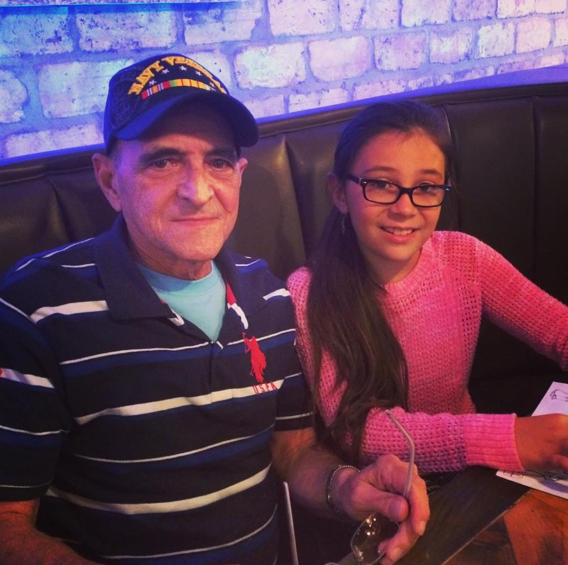 A grandfather and his granddaughter share a joyful moment at a restaurant table while dining.