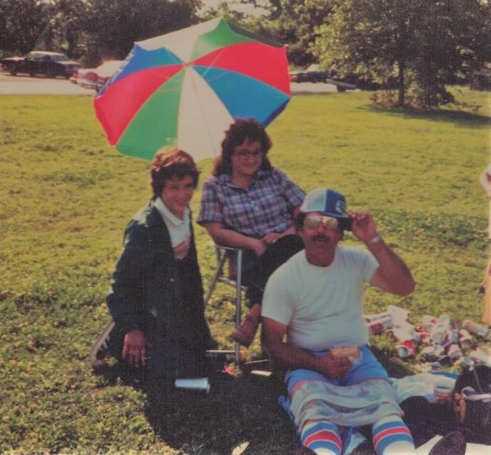 Three people relax on the grass under a vibrant umbrella, sharing a fun afternoon together.