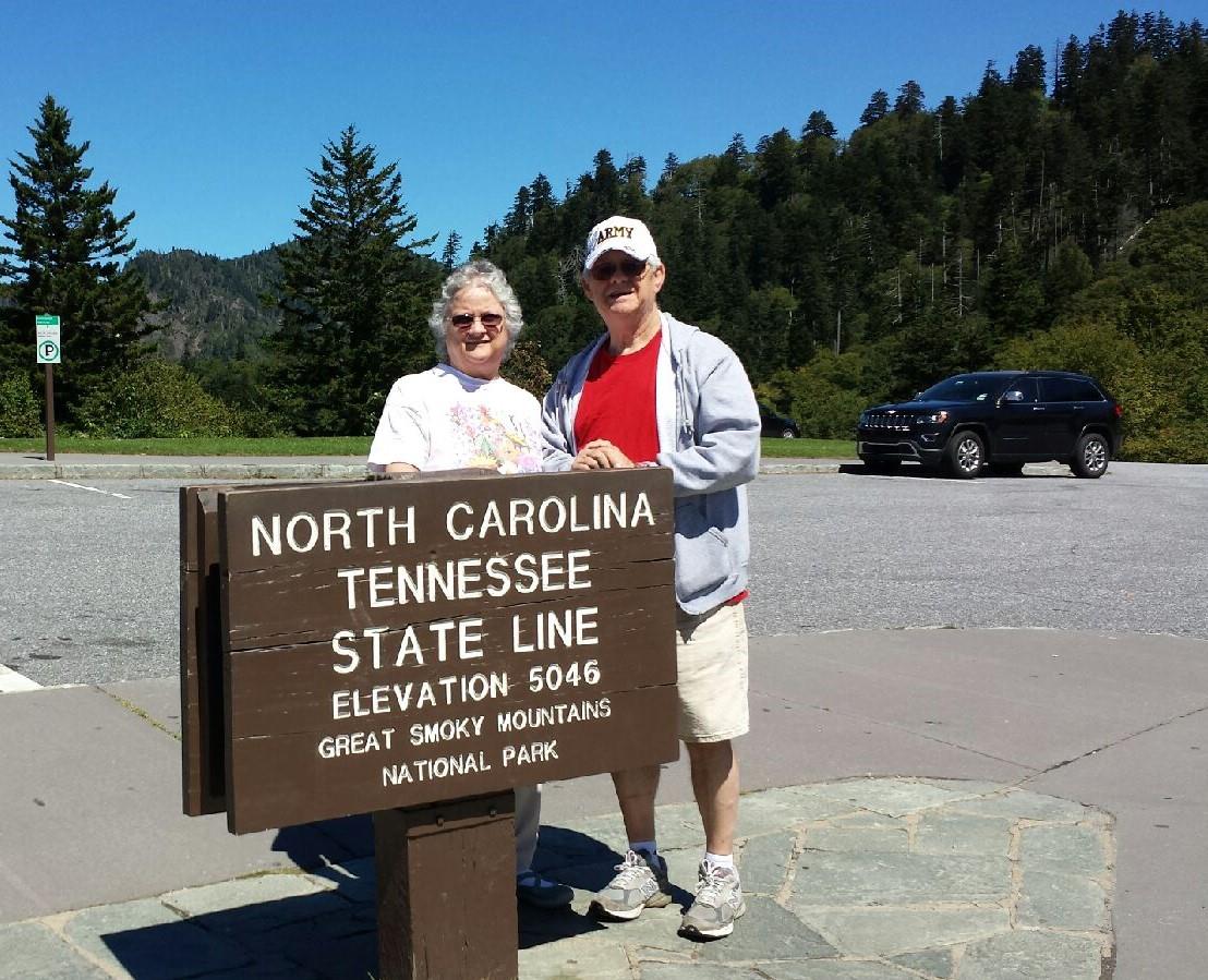 Two people stand happily at the North Carolina and Tennessee border in Great Smoky Mountains.