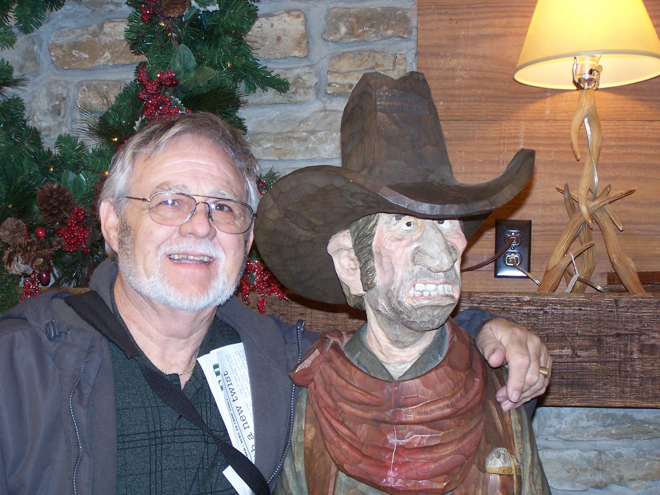 Friendly interaction captured between a man and a wooden cowboy figure in a decorated venue.