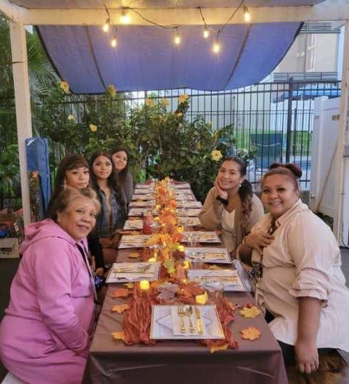 Six people enjoy a festive meal together at a beautifully set outdoor table decorated for autumn.