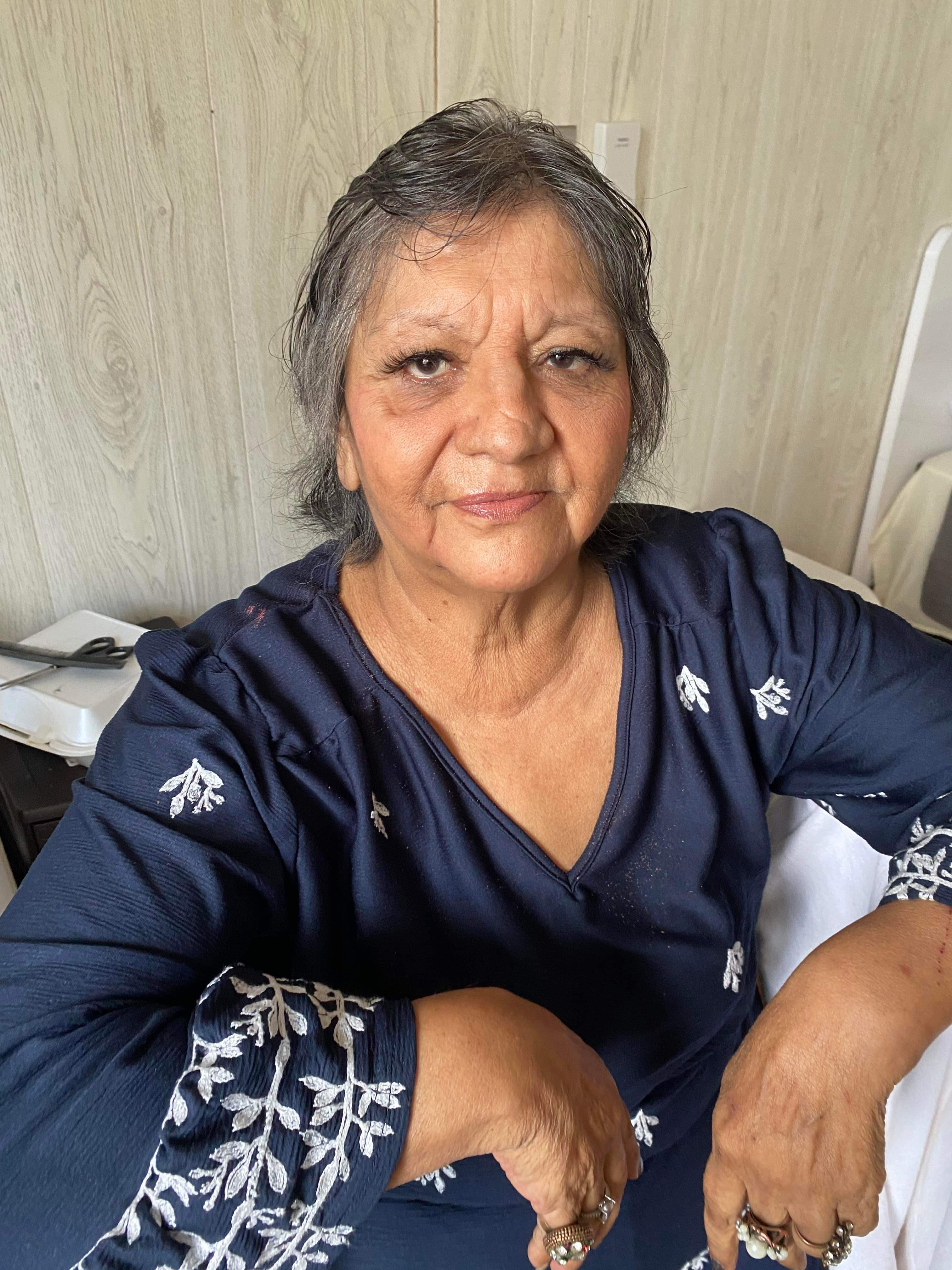 An elderly woman poses for a portrait with a warm smile while seated at home.