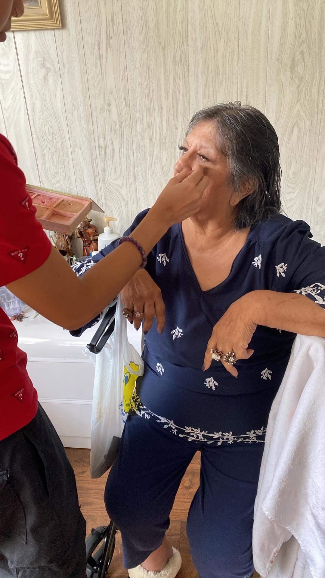 Family member helps elderly woman apply makeup in a cozy home environment, promoting bonding.