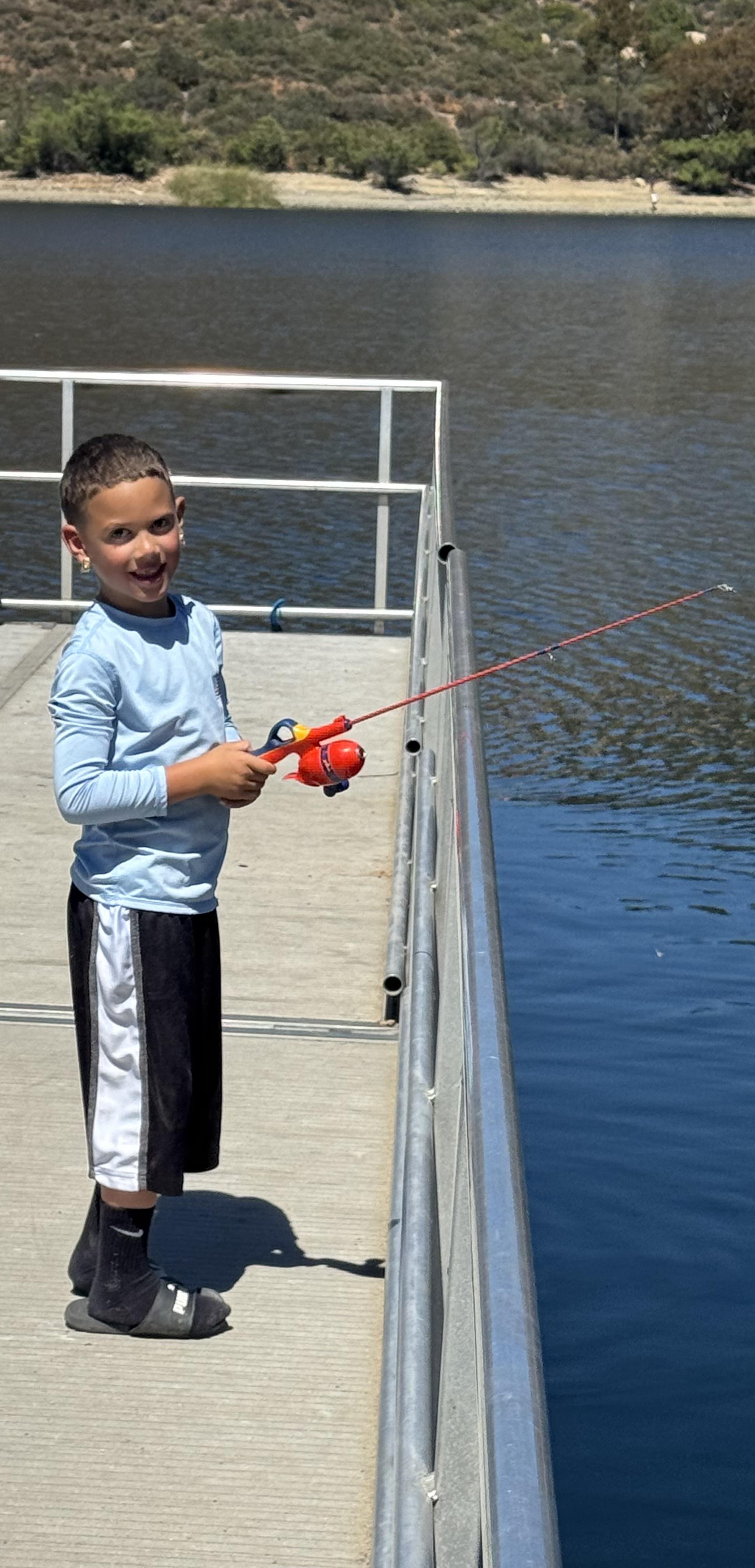Child happily casts a line while fishing from a dock, enjoying quality time outdoors.