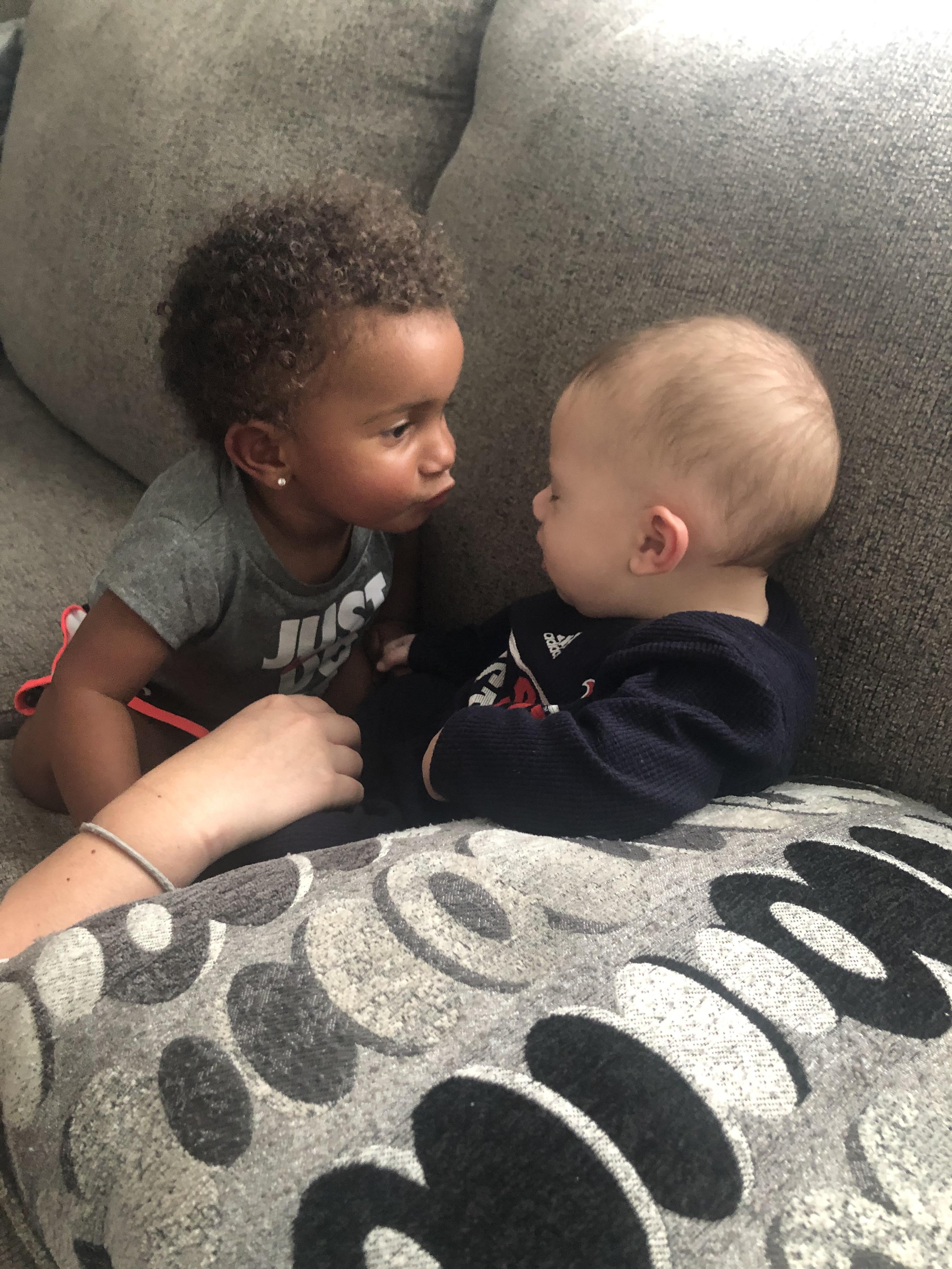 Two young children engage in a playful interaction on a comfortable couch at home.