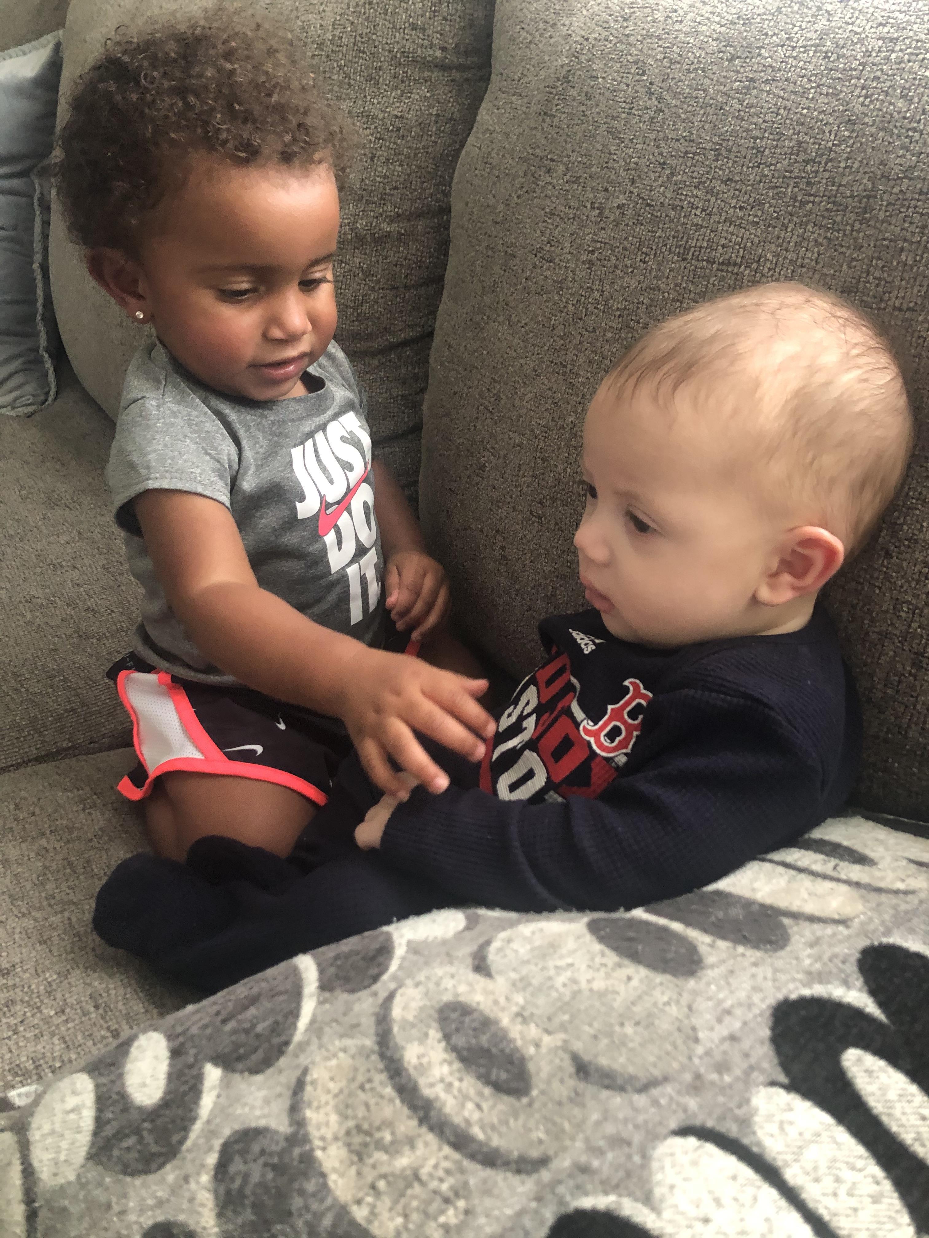 Two young children enjoy each other's company on a comfortable couch in a living room.
