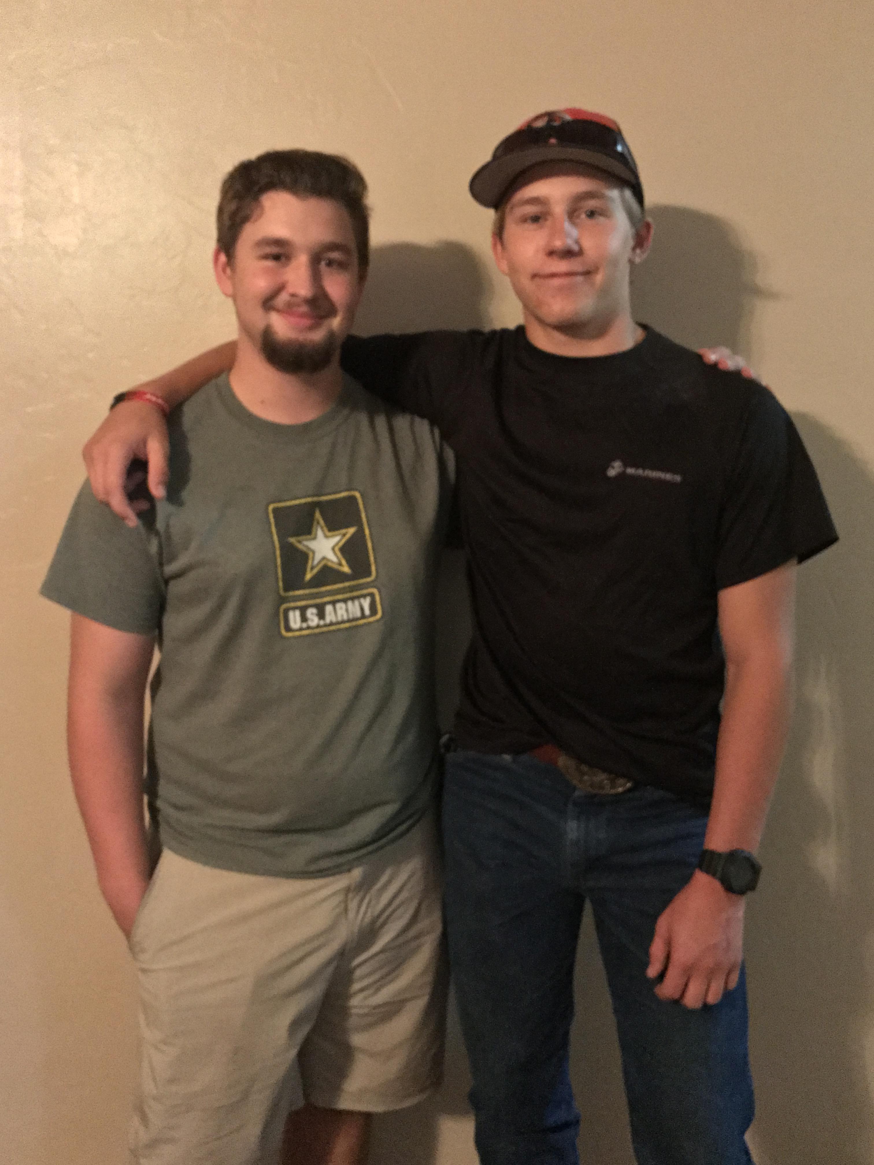Two friends stand side by side, smiling happily in casual outfits in a warm indoor setting.