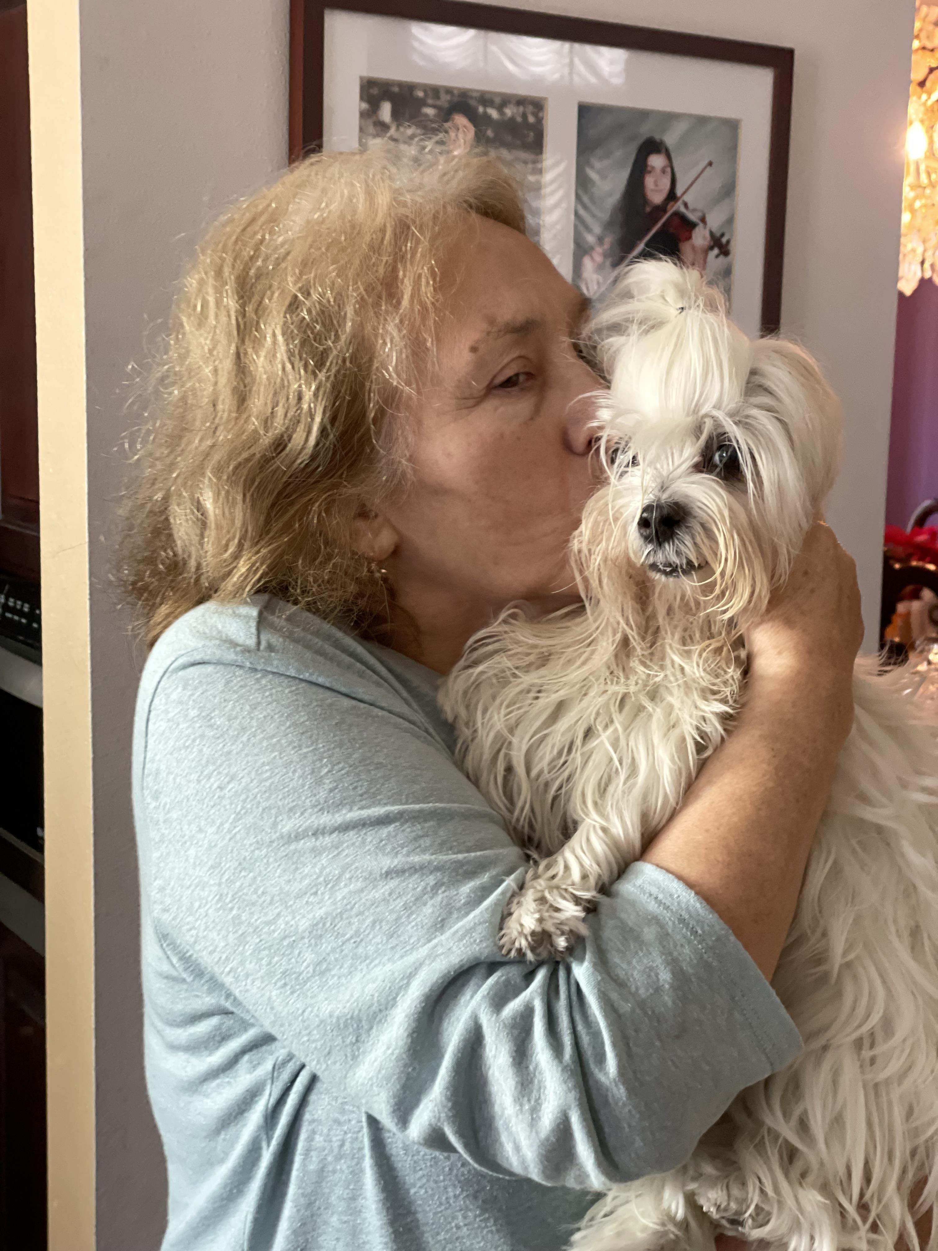 A woman shows love to her small white dog in a warm indoor environment, enhancing their bond.