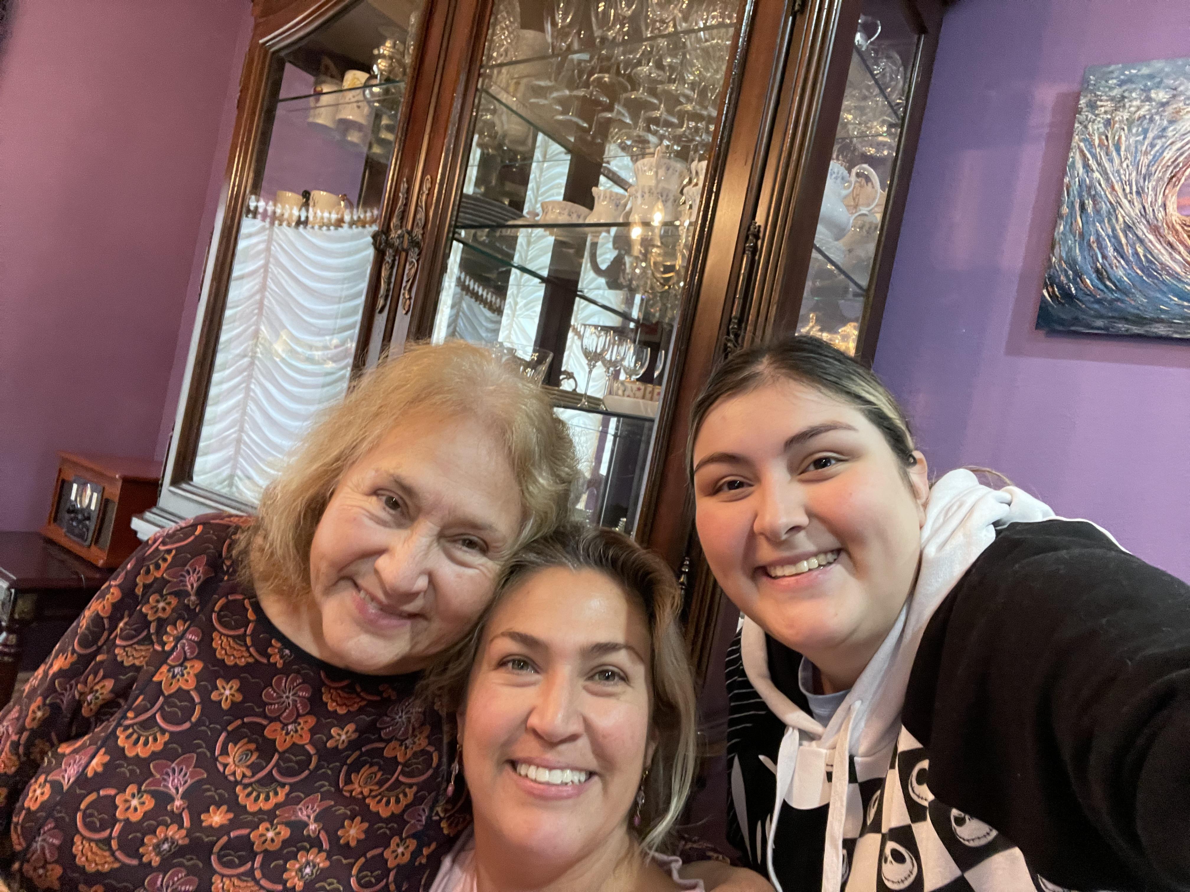 Three women smile together in a warm, inviting living room filled with colorful decor.
