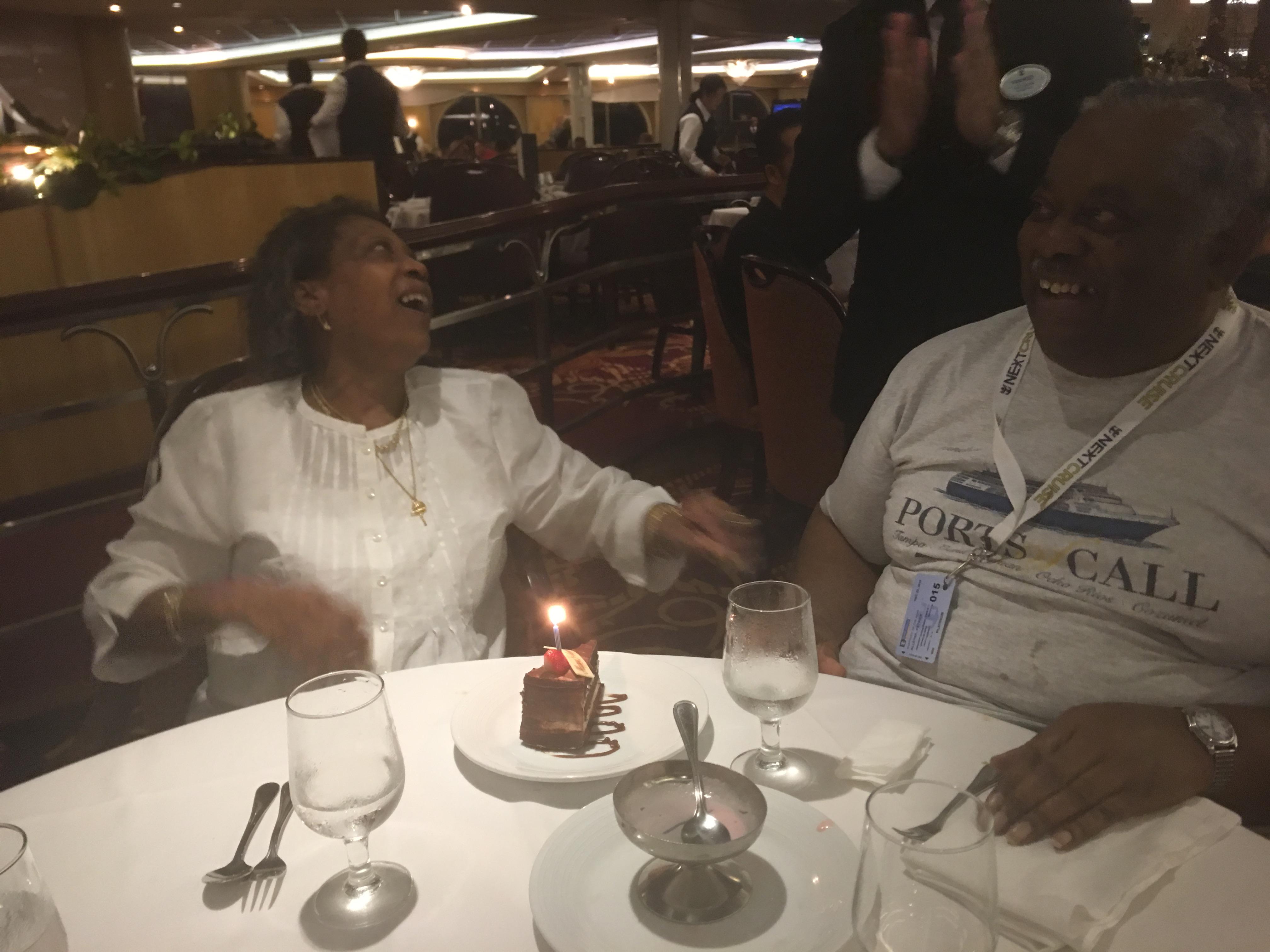 Two people share joy and laughter over cake at a birthday celebration on a cruise ship.