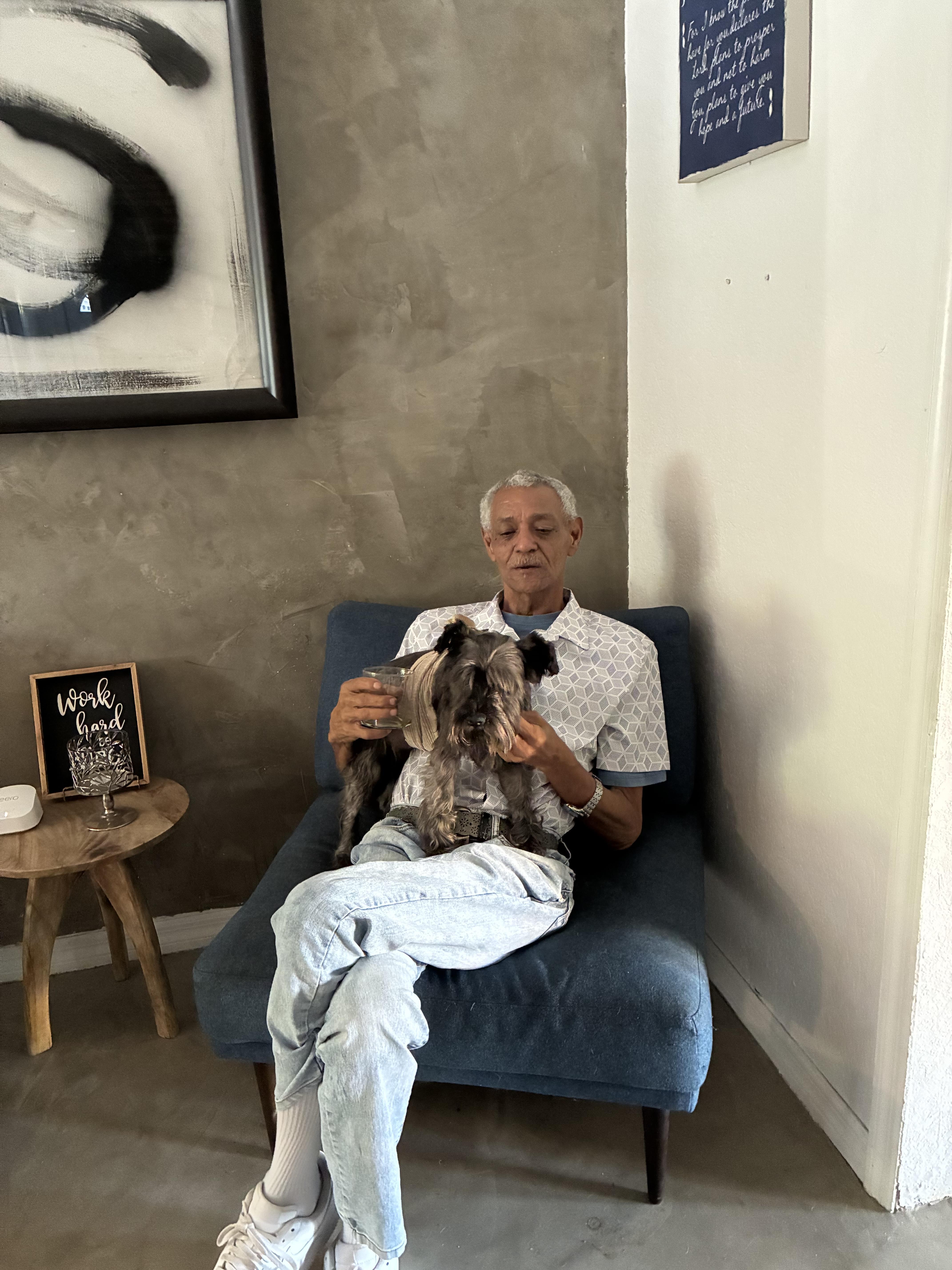 An elderly man relaxes in a chair, holding a small dog in a cozy, stylish room.