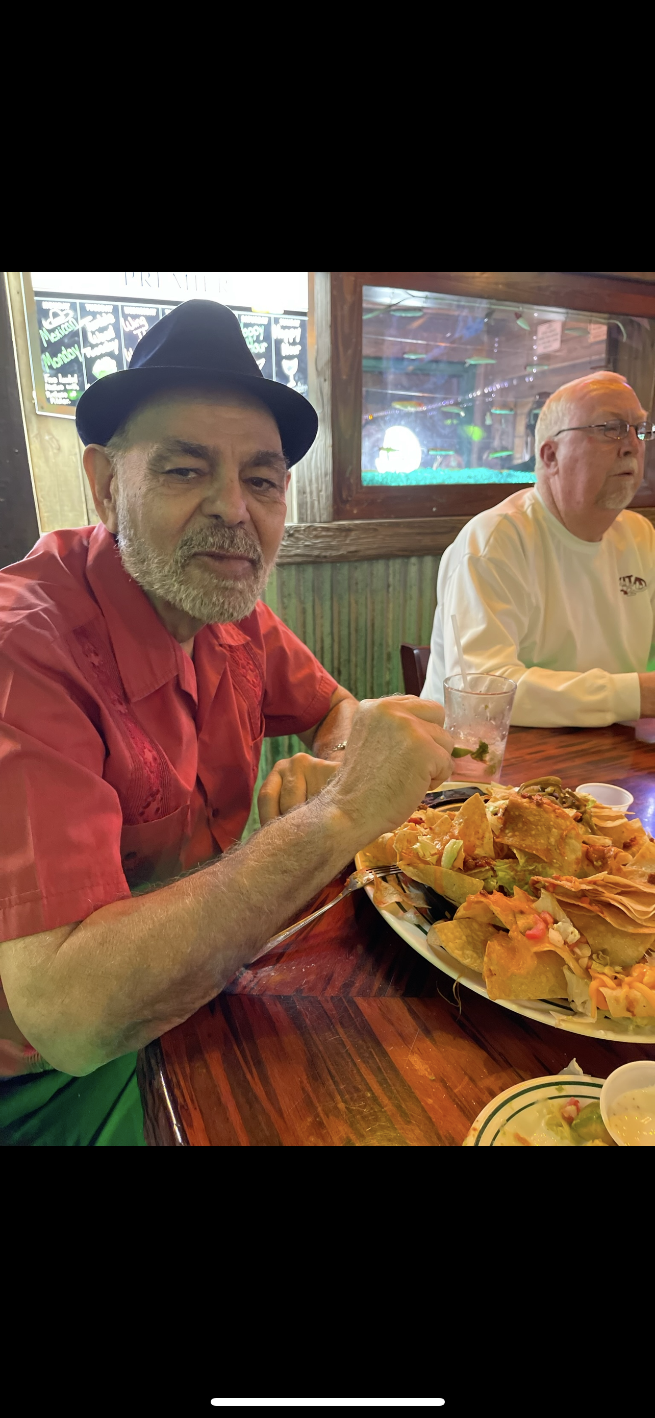 Two friends sit together at a table, enjoying a large plate of nachos with drinks.