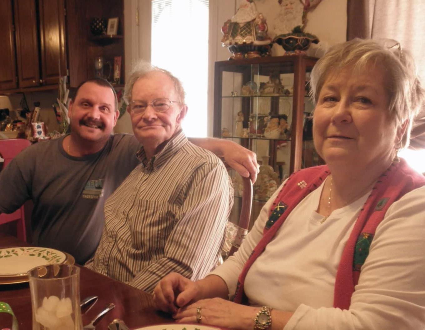 Three family members enjoy each other's company around a dining table, sharing stories and smiles.