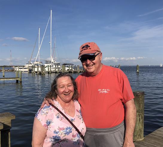 A man and woman standing on a dock with boats in the background