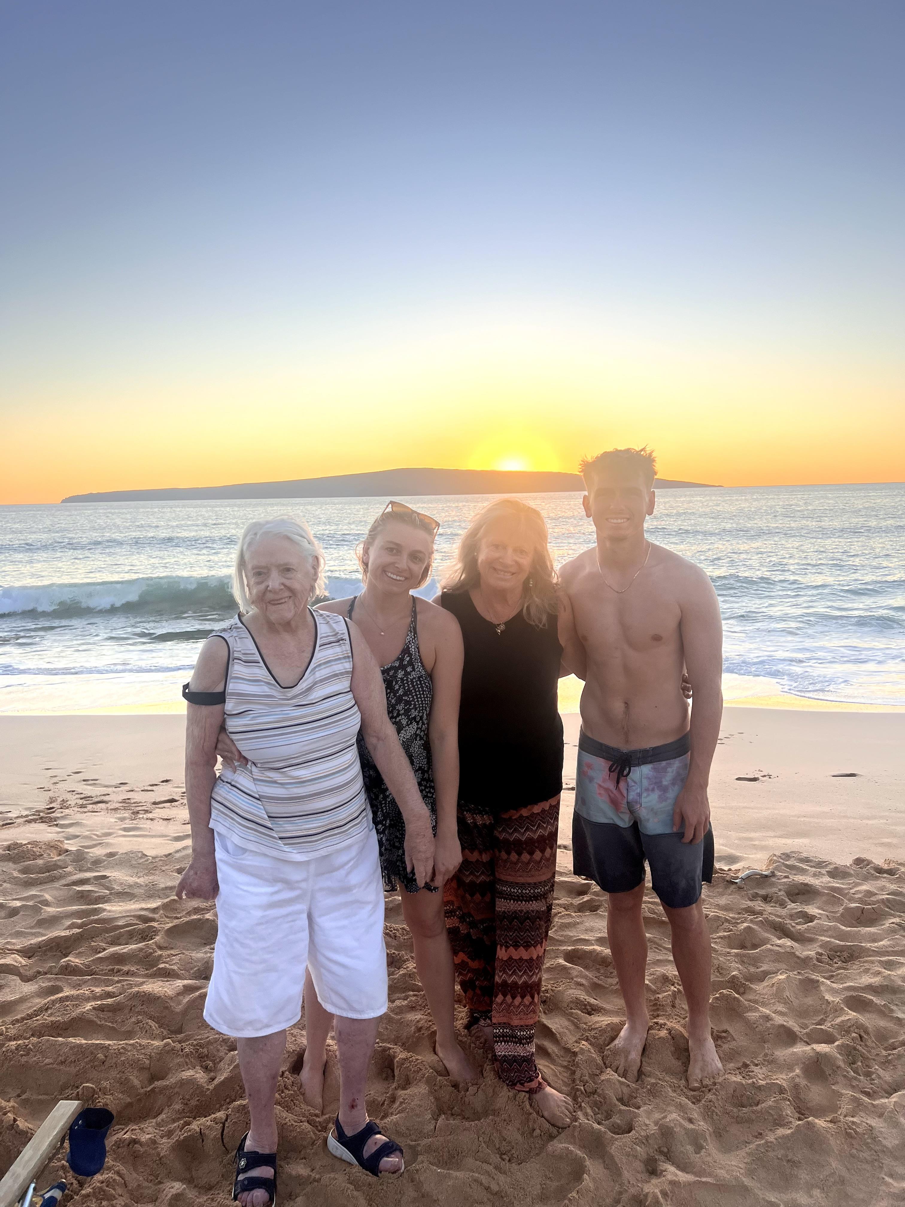 Four family members stand on the sand during sunset, enjoying a peaceful moment by the ocean.