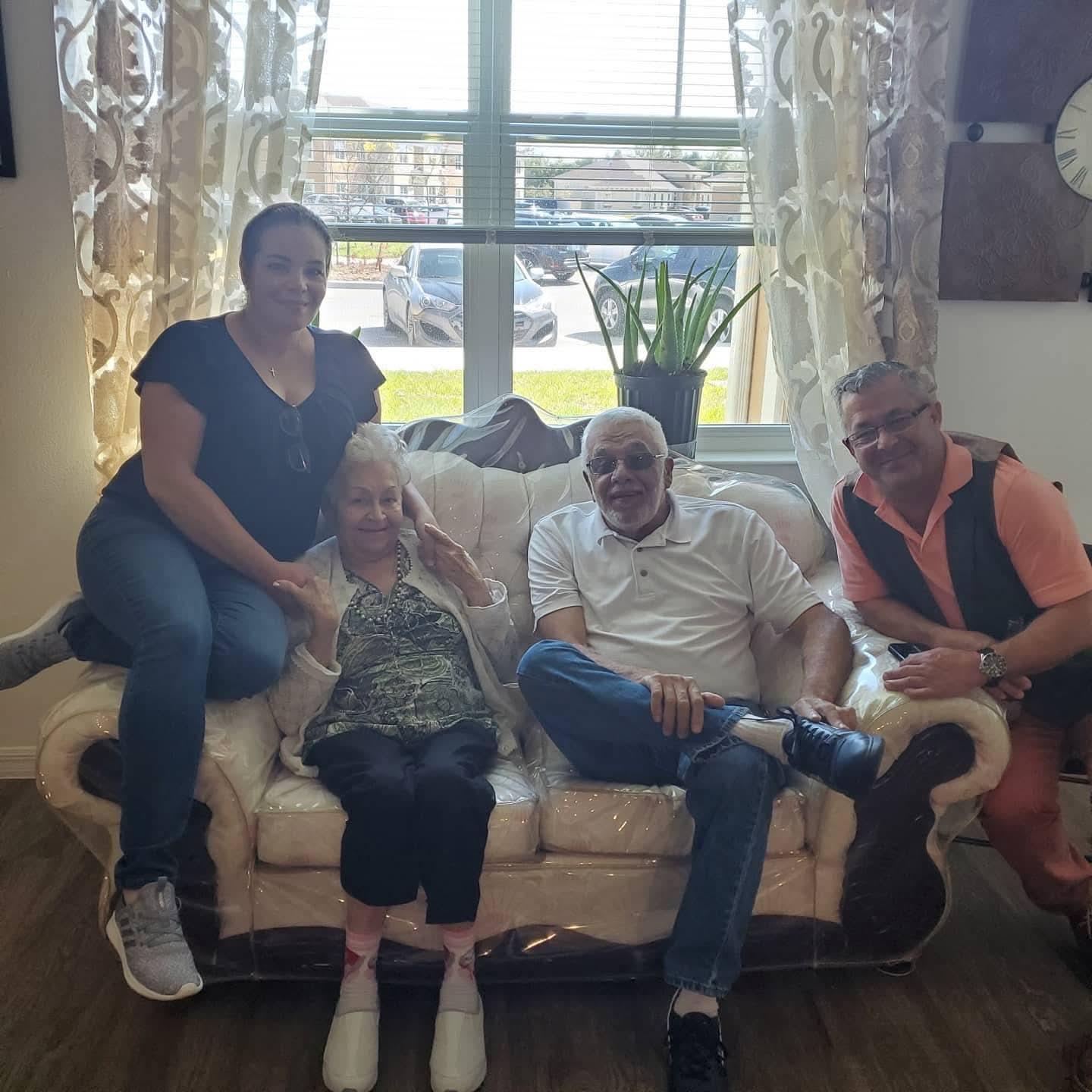 Four family members sit comfortably on a sofa, sharing smiles in a warm living room.