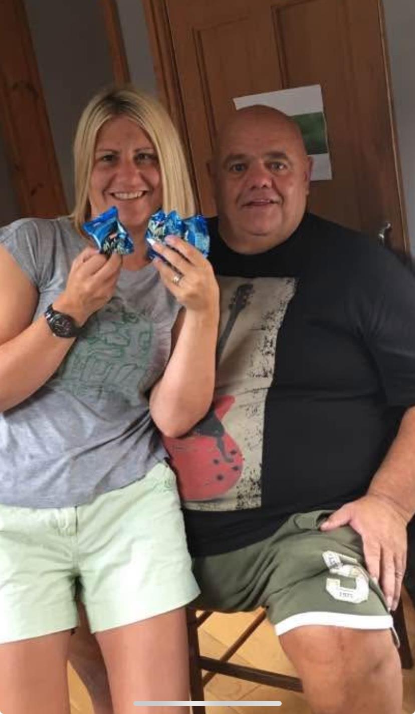 Two people smiling and holding snacks while sitting closely in a relaxed home environment.