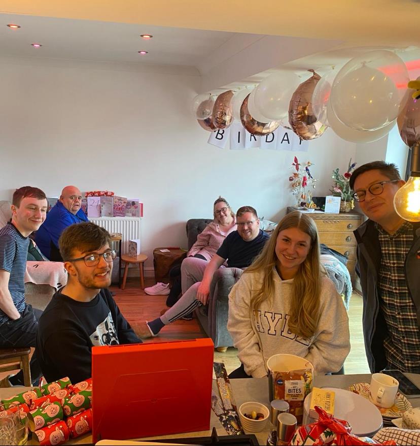 Friends gather in a cozy room to celebrate a birthday, surrounded by decorations and gifts.