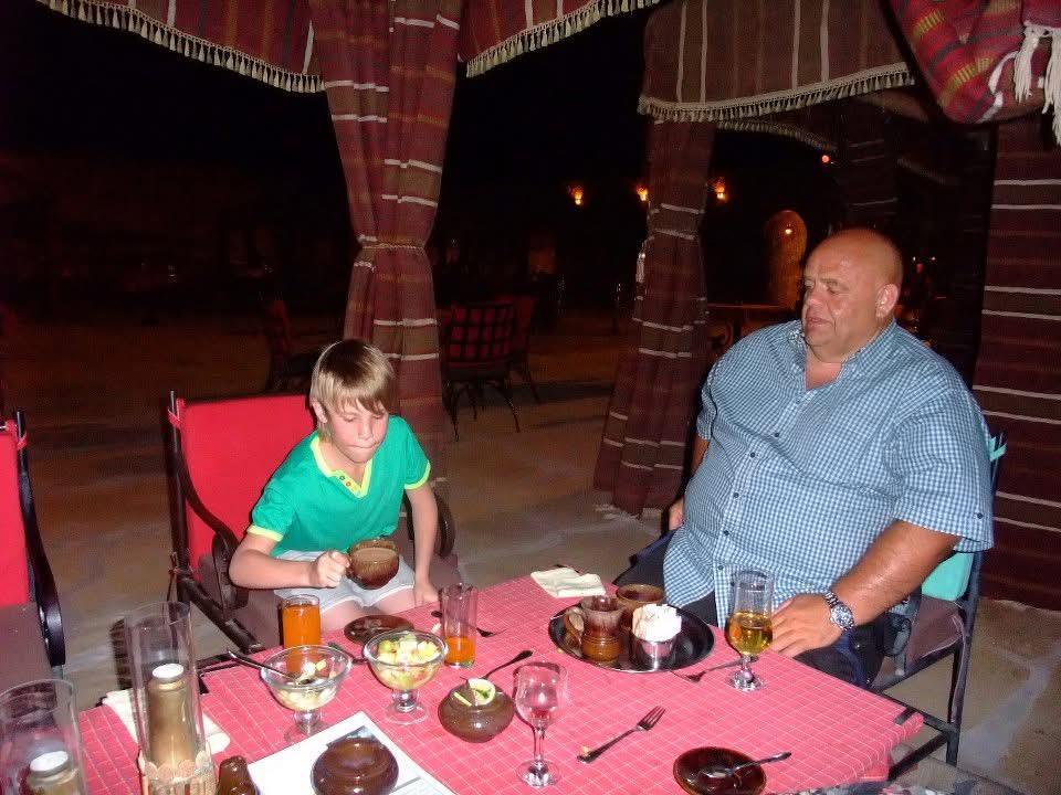 A man and a boy enjoy traditional cuisine at a desert resort during an evening gathering.