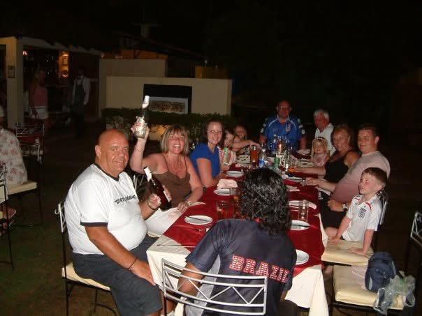 Friends and family share a joyful dinner outdoors at night, enjoying each other's company.