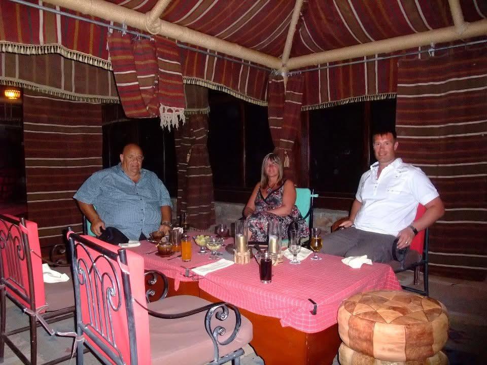 Friends gather around a table for dinner in a comfortable outdoor tented area at night.