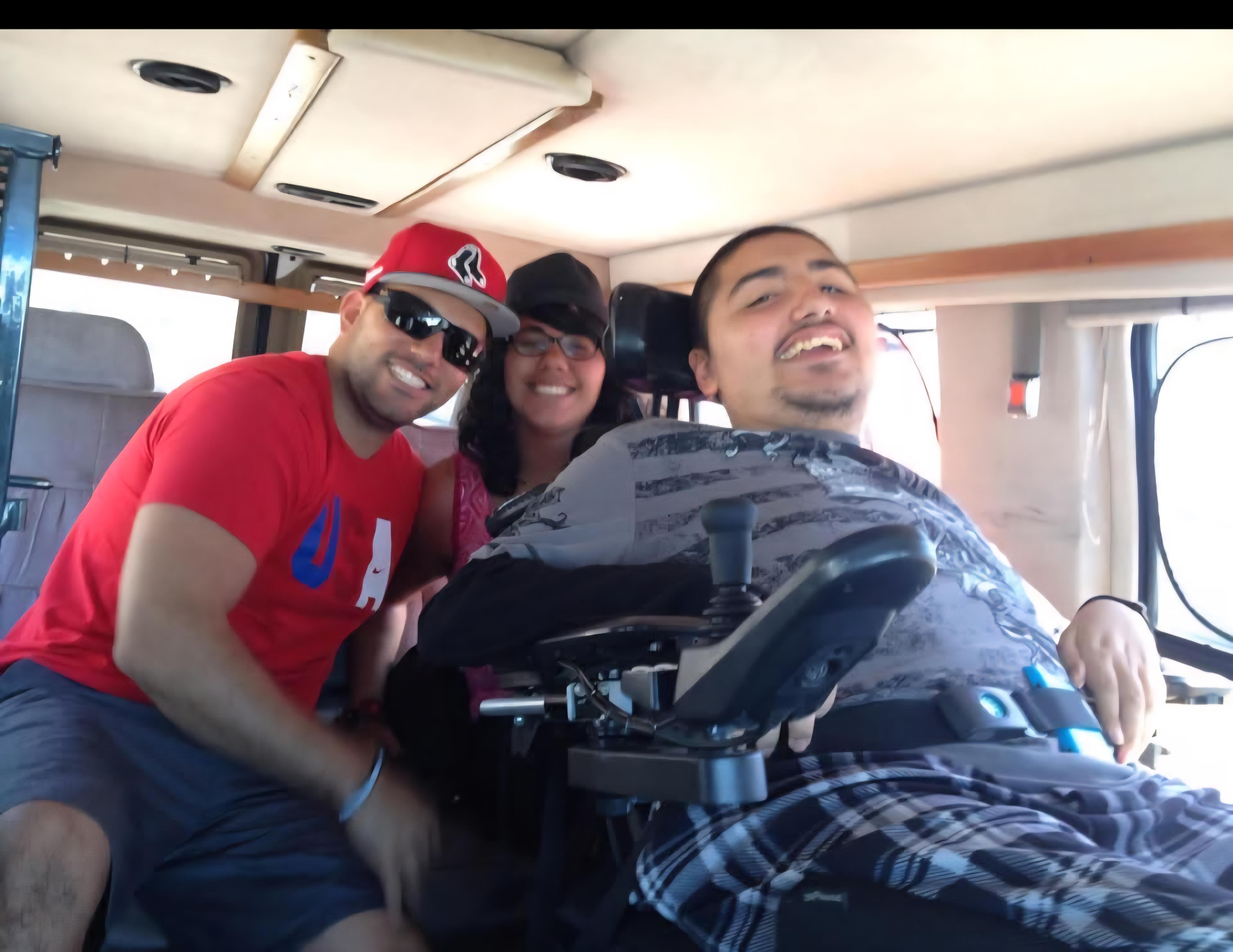 Three people relax together in a van, sharing smiles and laughter on a sunny day outside.