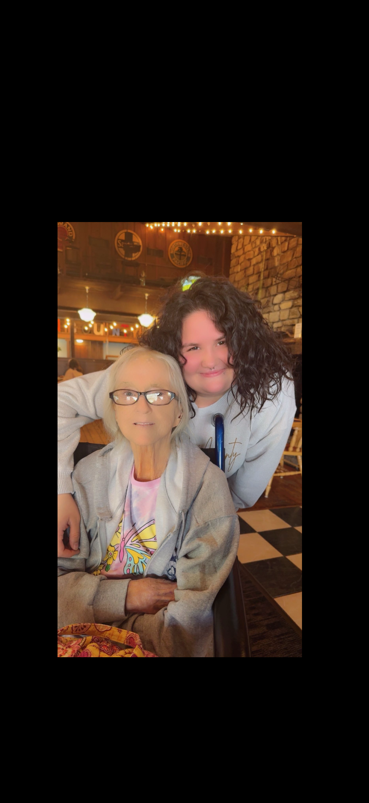 Two women are smiling and posing together in a cozy café, creating a warm atmosphere of friendship.