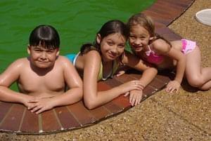 Two children play near a green pool, smiling and having fun on a warm sunny day.
