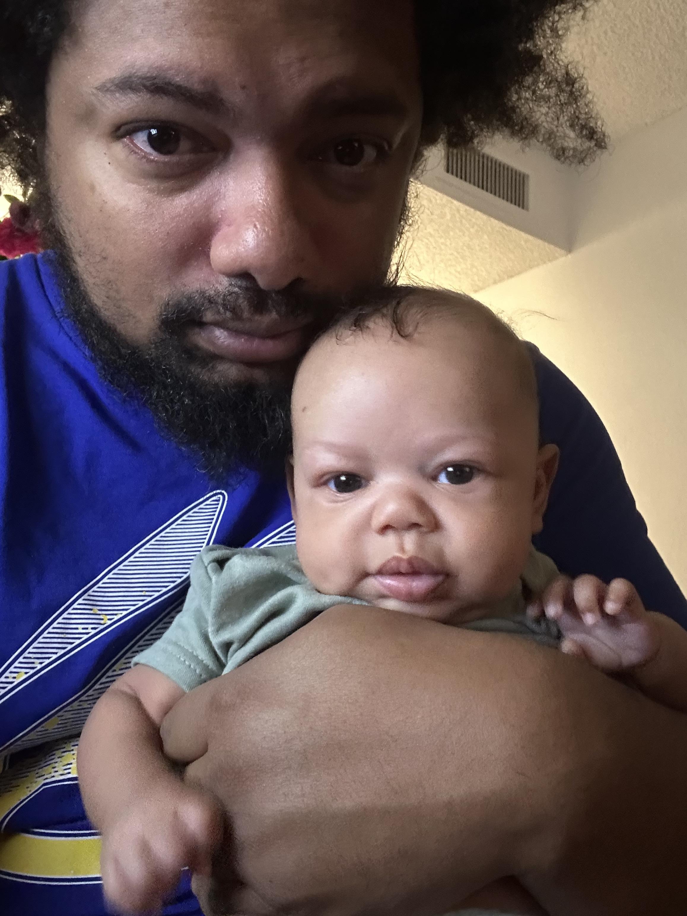 A father holds his infant child in a cozy room, emphasizing their bond and intimacy.