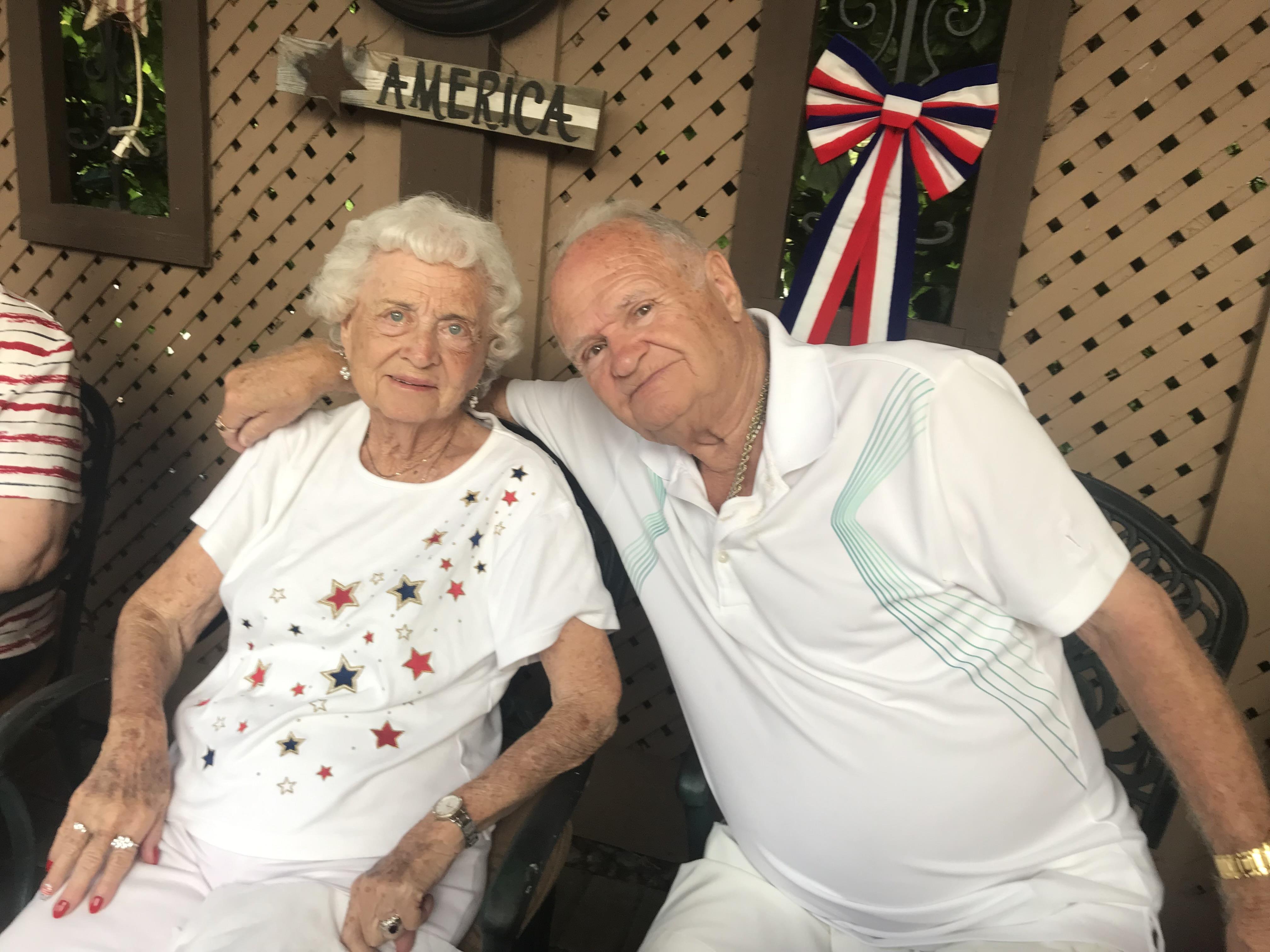 Two senior individuals sit closely, smiling and enjoying each other's company at a summertime event.