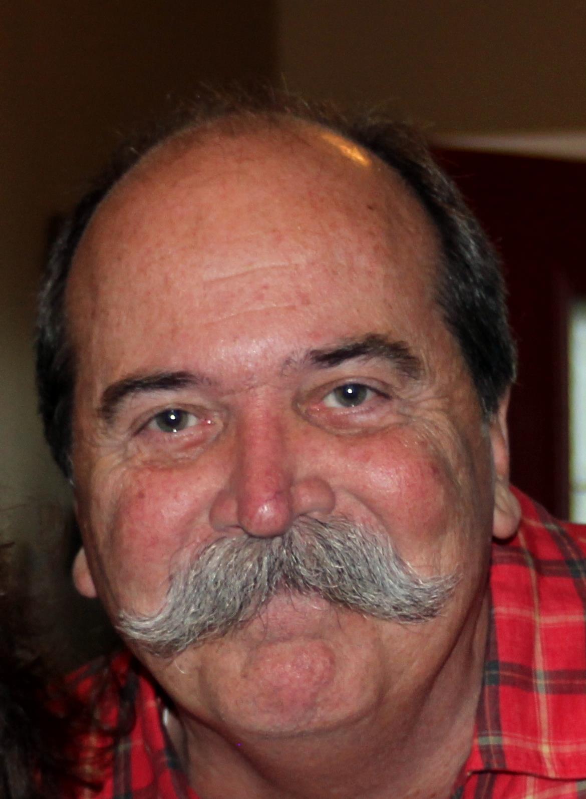 A cheerful man with a prominent mustache enjoys a friendly moment in a cozy indoor setting.