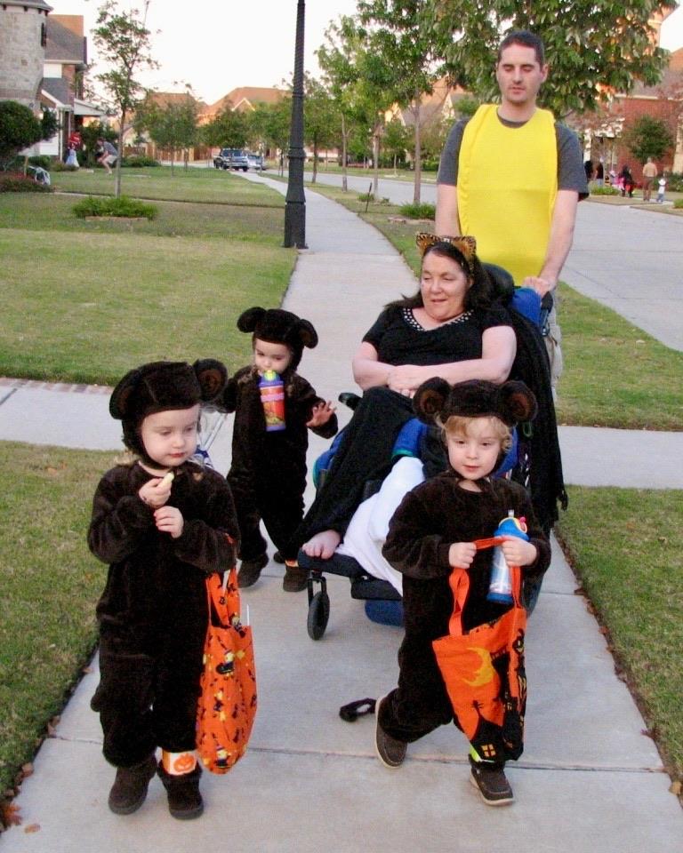 A family walks through their neighborhood as children dressed in bear costumes hold snacks and bags.