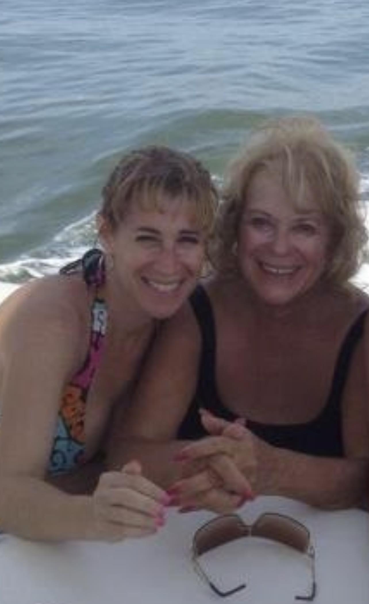 Two women share laughter and joy while enjoying a sunny boat ride on serene waters.