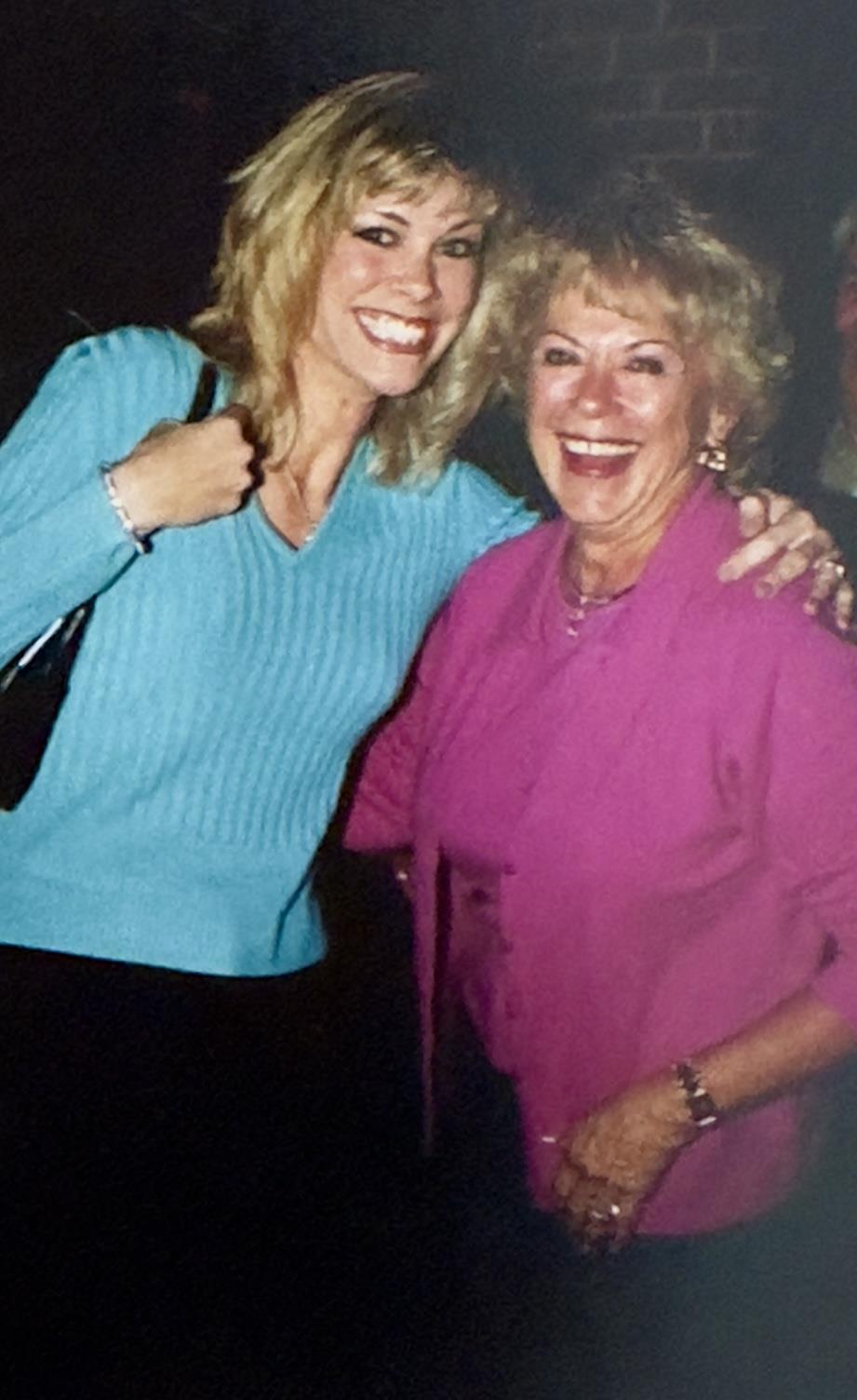 Two women share a happy moment, smiling and embracing each other at a vibrant gathering.