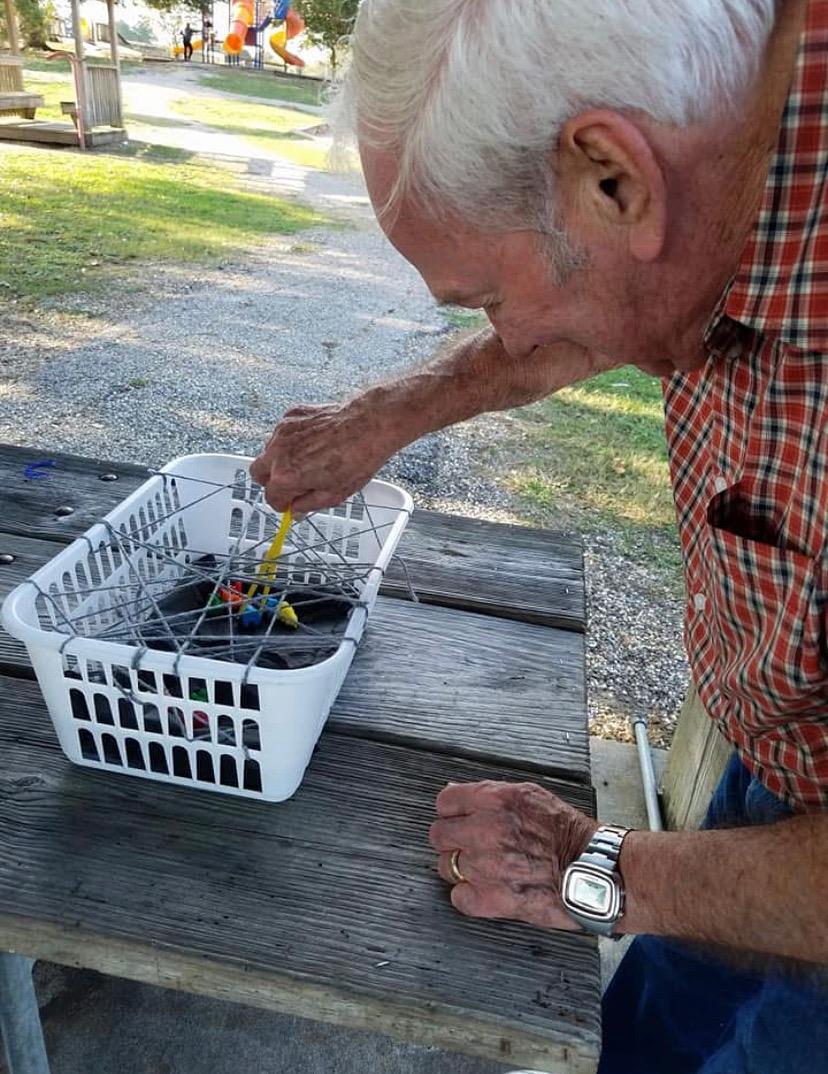 Senior man concentrates while arranging vibrant items inside a basket on a park table.