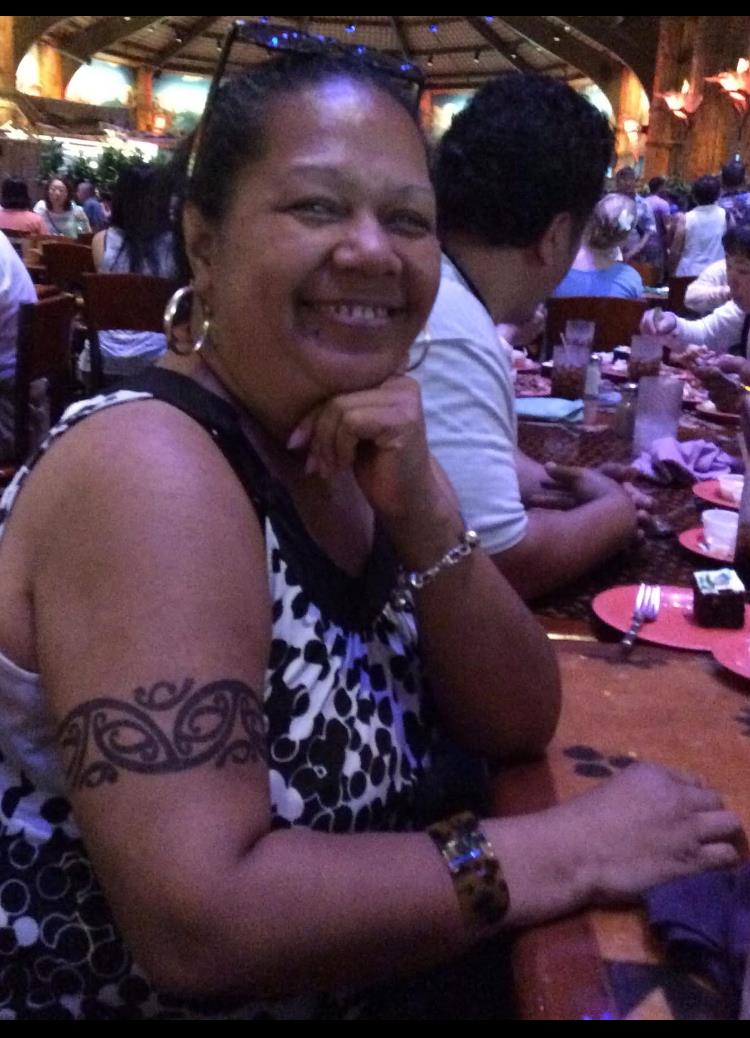 A woman smiles while dining with friends in a vibrant restaurant atmosphere, showcasing her tattoo.