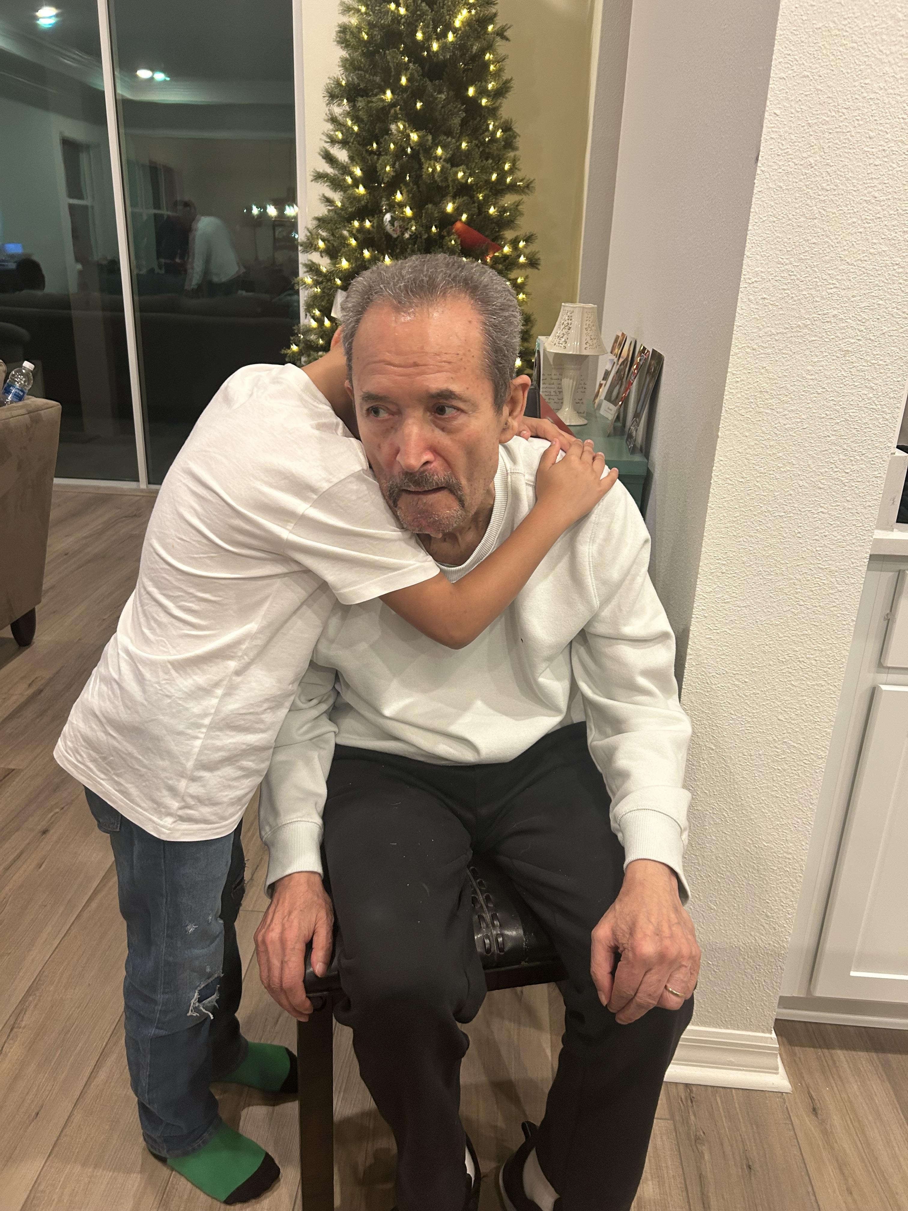 Holiday gathering captures a child affectionately hugging an older man in a warm atmosphere.