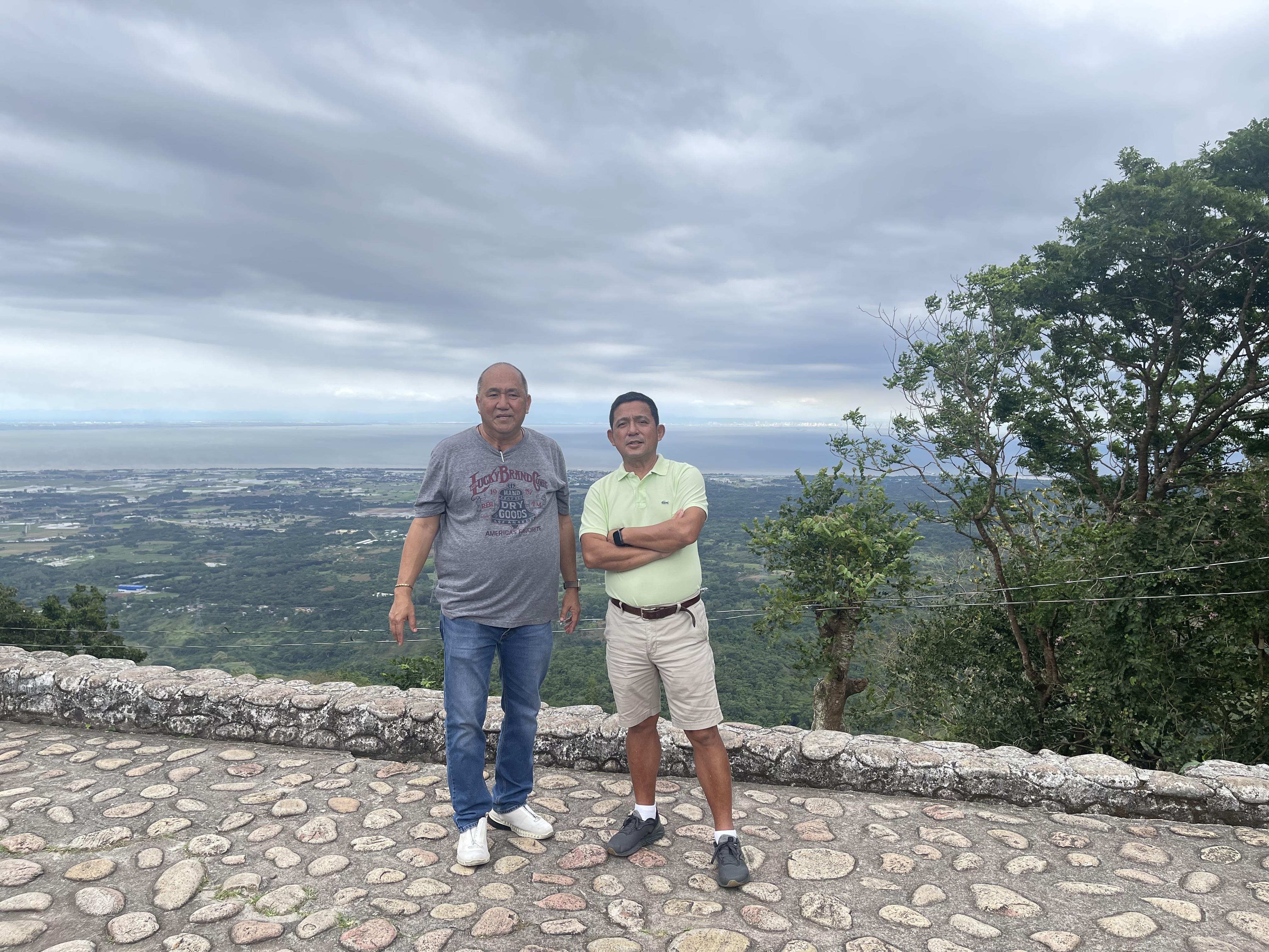 Two individuals pose next to each other on a stone path, enjoying a panoramic view of the valley.