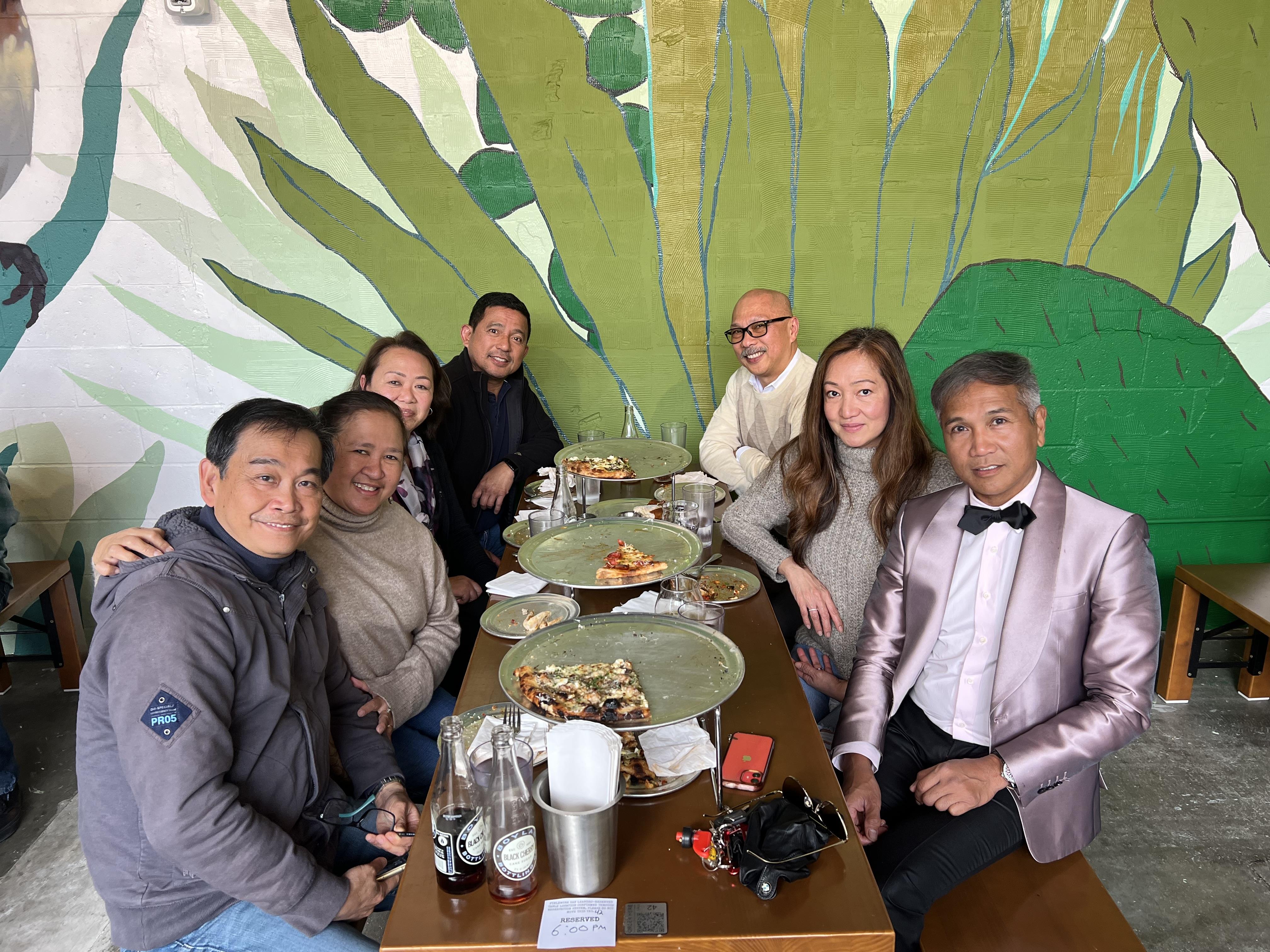Friends share laughter and delicious pizza while seated at a vibrant restaurant table.