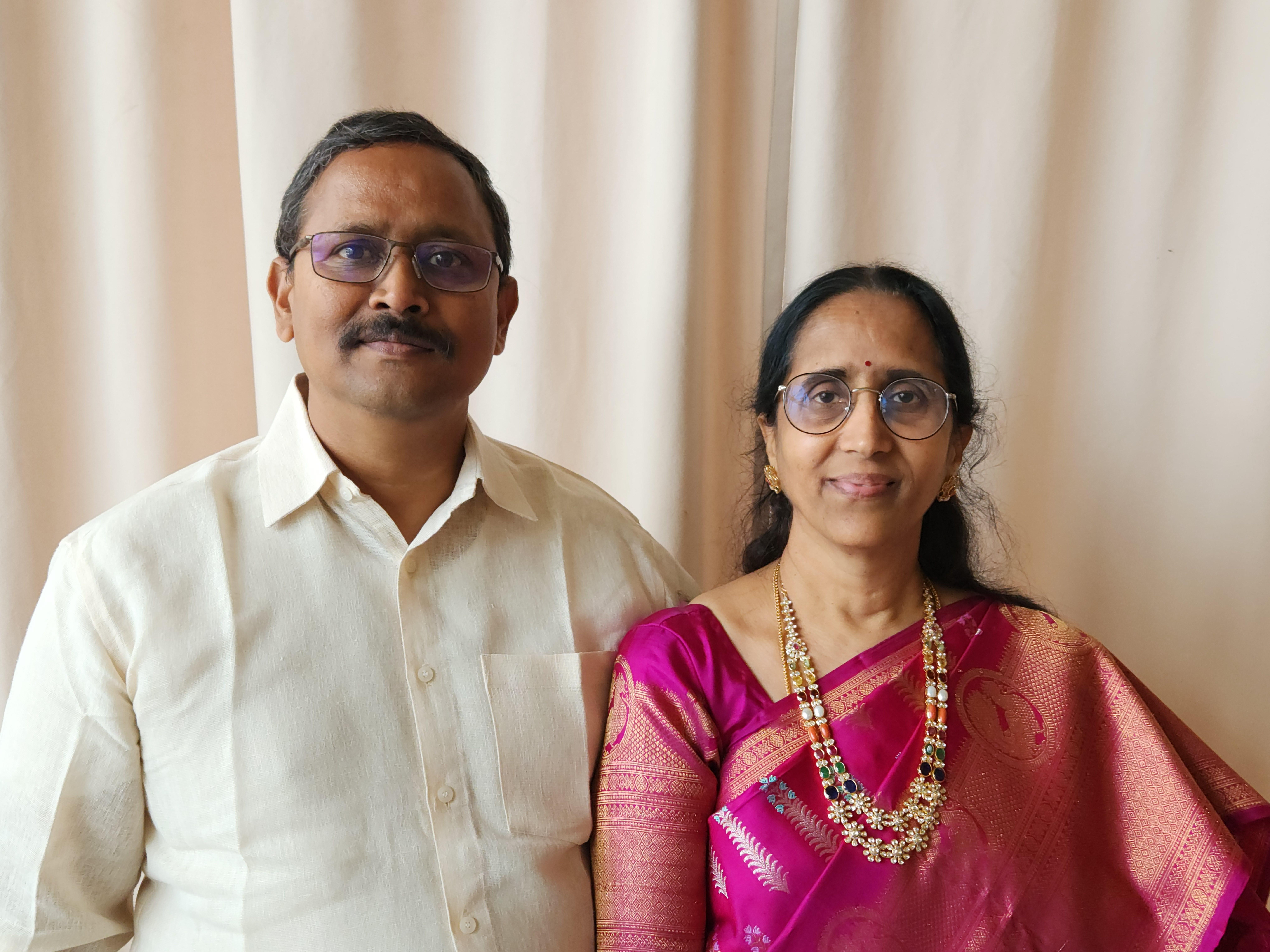 A man and woman in traditional attire smile at an evening cultural gathering.