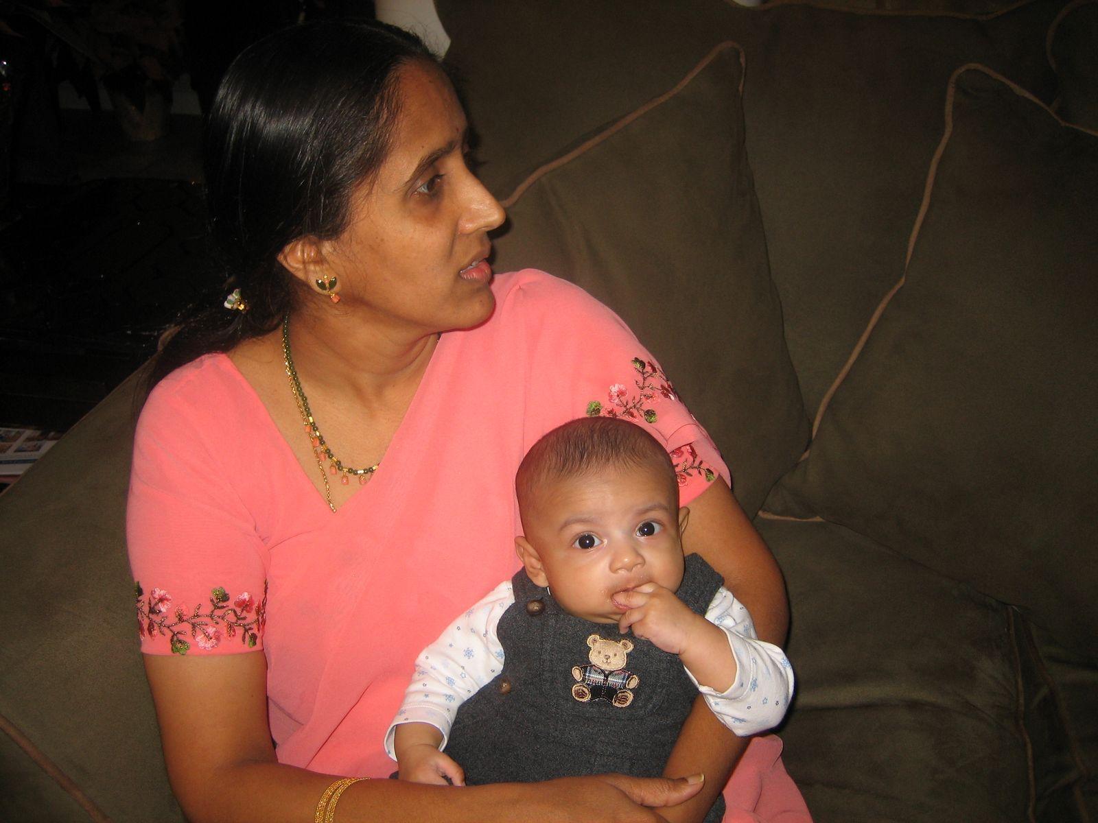 A woman in a pink sari gently holds a baby in a casual setting, sharing a tender moment.