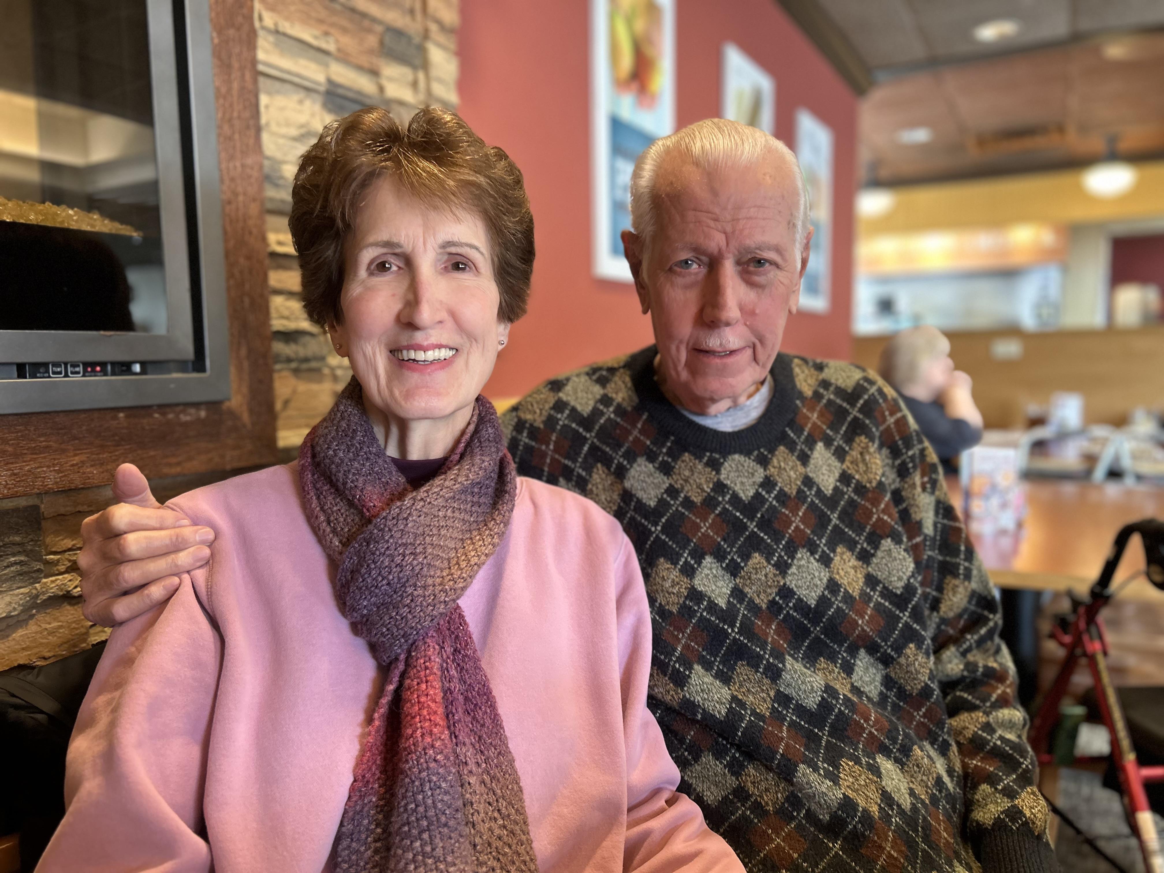 Two seniors share smiles while sitting together in a cafe, enjoying their time and warmth.
