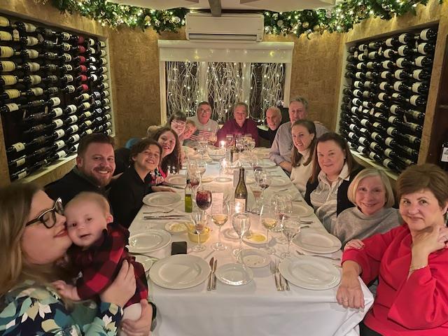 A large family enjoys a dinner together at a warmly decorated restaurant table filled with food.