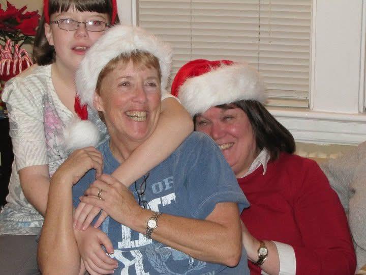 Three family members share a moment of happiness while wearing Santa hats and smiling together.