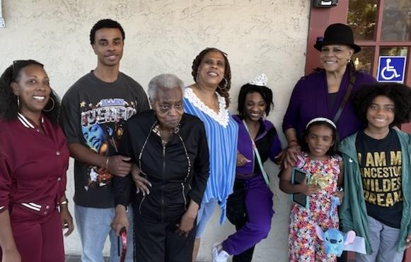 A joyful group of family members poses together, celebrating their bond in a sunny outdoor setting.