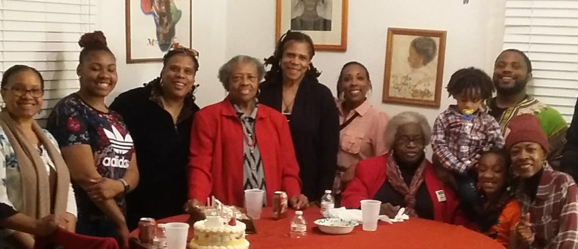 Family members gather around a red table to celebrate an anniversary with joy and cake.